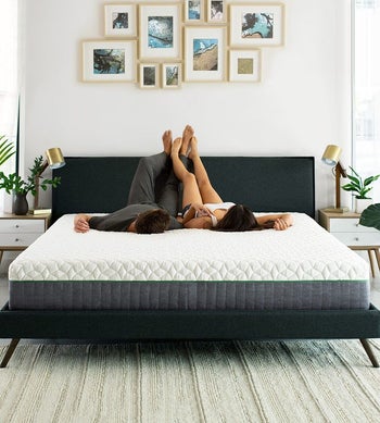 two models lying on a mattress on a bed frame with their feet against the headboard