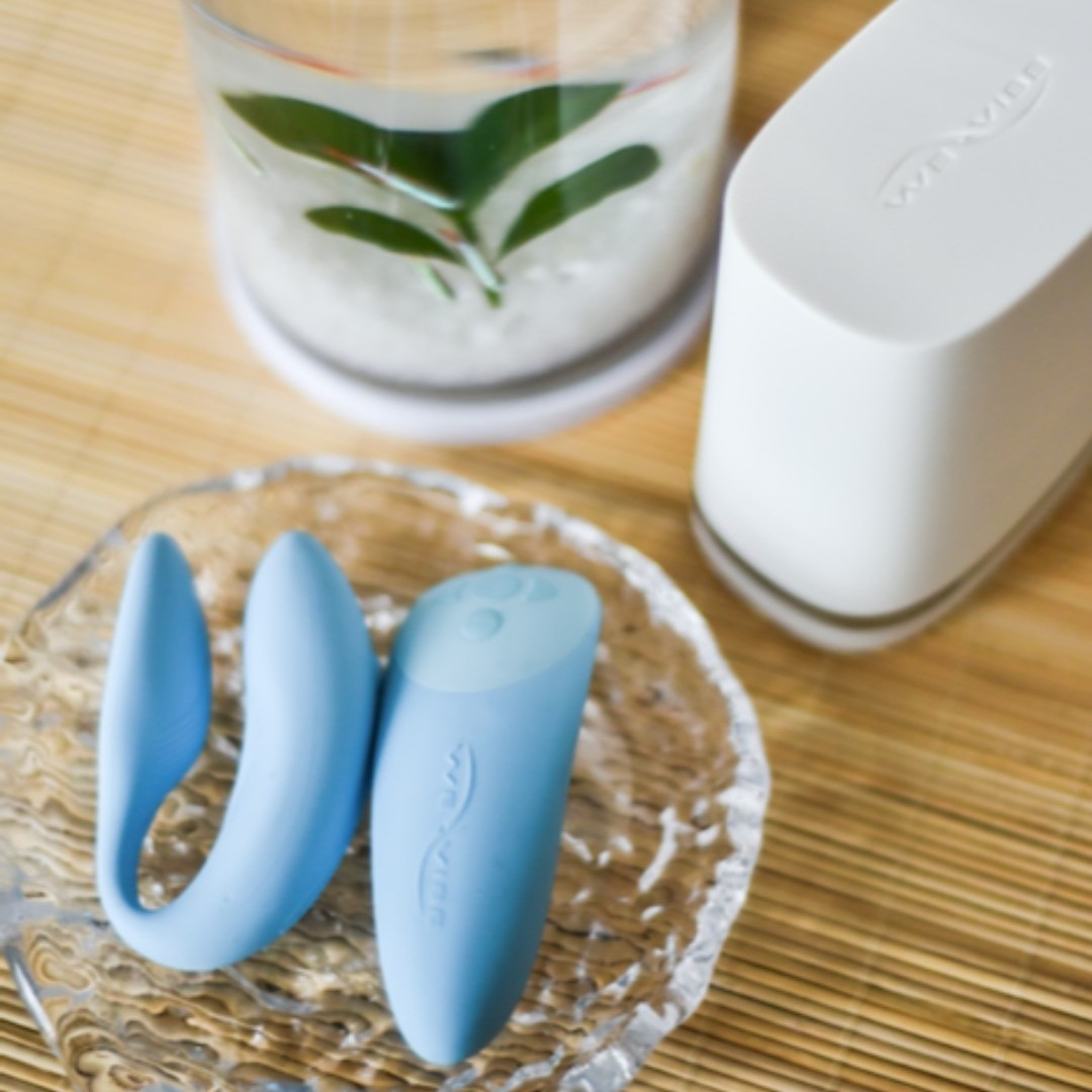 Blue dual stimulator and wireless remote next to white charger base