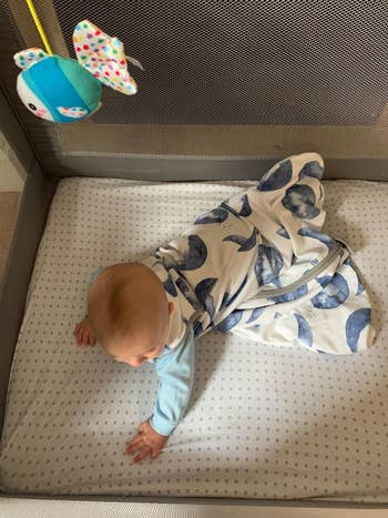 a reviewer photo of a baby crawling while wearing the sleep sack