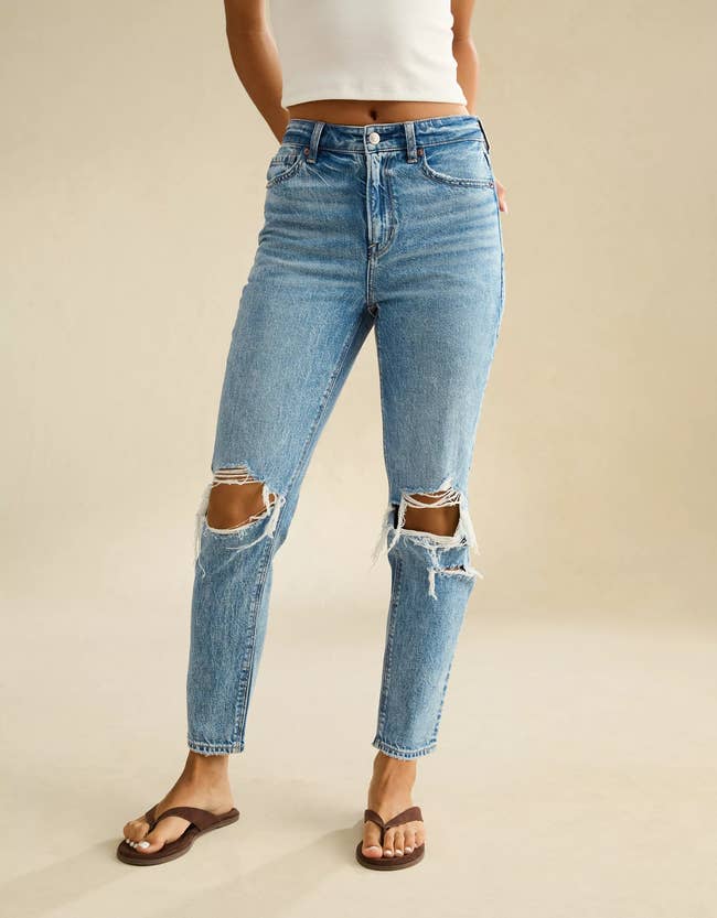 Person wearing high-waisted ripped jeans and a sleeveless top, paired with sandals, showcasing casual attire