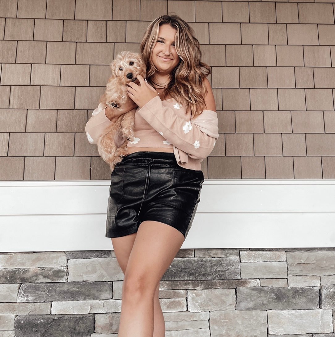 buzzfeed writer in mid-thigh-length faux leather paper bag shorts holding a puppy