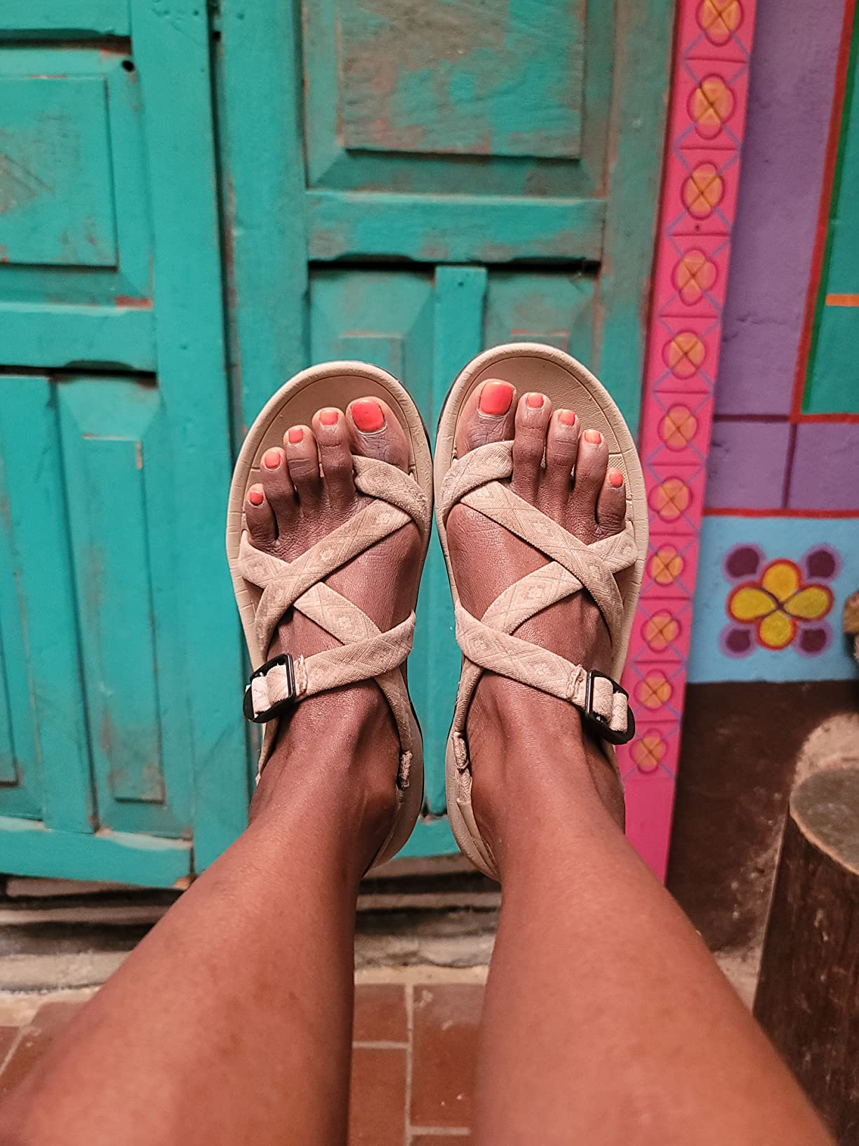 Person wearing strappy sandals with buckles, showing painted toenails, successful  beforehand   of a vibrant, patterned doorway  background