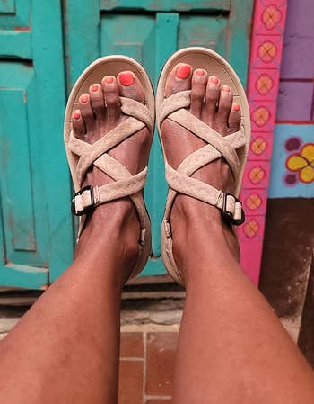 Person wearing strappy sandals with buckles, showing painted toenails, successful beforehand of a vibrant, patterned doorway background