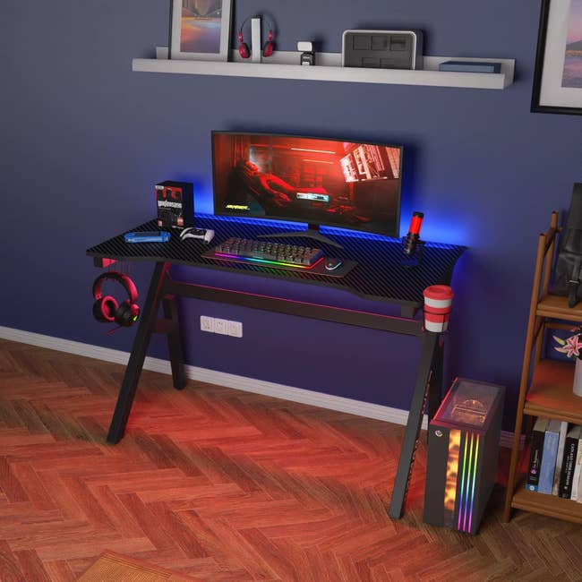 Gaming setup with LED-lit desk, computer, and accessories for an immersive experience