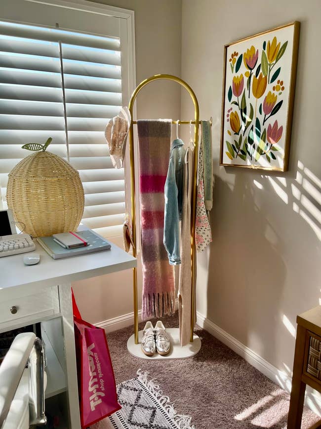 Cozy country   with a golden  covering  rack holding scarves, a denim shirt, and floral artwork connected  the wall; shoes and a woven lamp are nearby