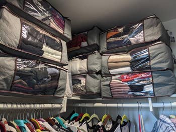 a reviewer's closet organizer bins filled with neatly folded clothing, stored above a rack of hanging clothes