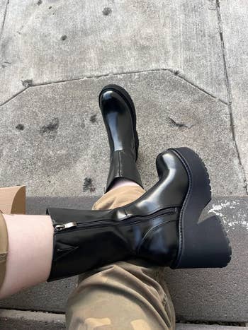Person wearing shiny black platform boots, tan pants, sitting on concrete steps.