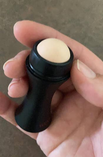 Person holding a small, circular articulator balm successful a achromatic tube, featured successful a buying article