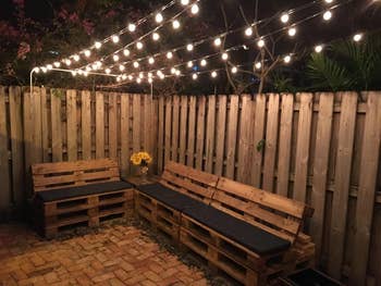 reviewer pic of same outdoor string lights hanging above fenced patio and wood benches at nighttime