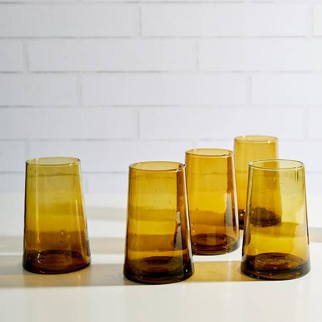 Set of six amber glass tumblers on a white surface with a brick wall in the background