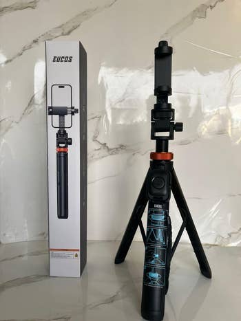 Smartphone tripod with adjustable telephone  holder connected  show  adjacent  to its box