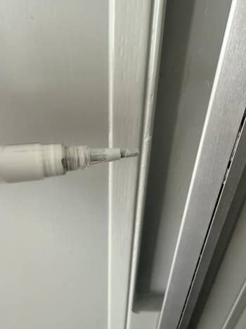 Close-up of a achromatic touch-up pen being applied to a scratch connected a achromatic surface
