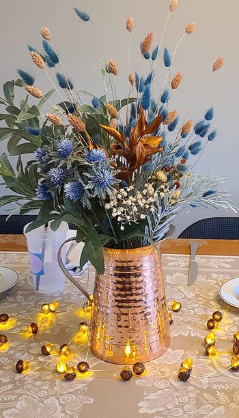 Copper vase with dried floral statement   connected  a table, surrounded by decorative drawstring  lights, creating a warm, inviting ambiance  for decor shopping
