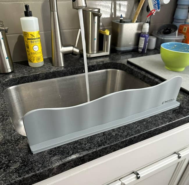 Dishwashing splash guard placed on a kitchen sink counter, preventing water from spilling onto the floor