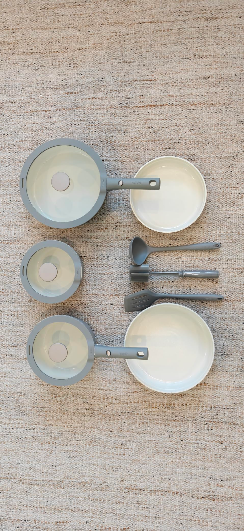 Cookware set with three non-stick pans, lids, bowls, and four utensils arranged neatly on a textured surface