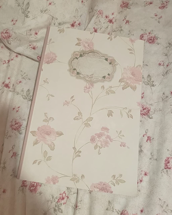 A small white notebook with pastel watercolor pink flowers on the front 