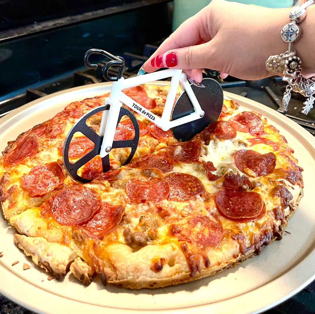 Reviewer cutting pizza with a white bicycle shaped spinning cutter with two blades as wheels 