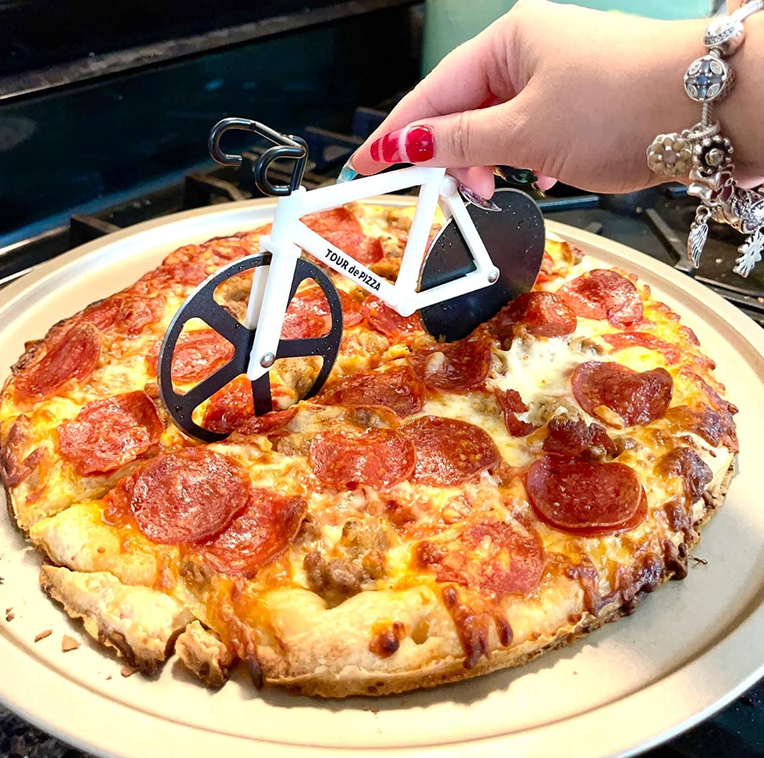 Reviewer cutting pizza with a white bicycle shaped spinning cutter with two blades as wheels 