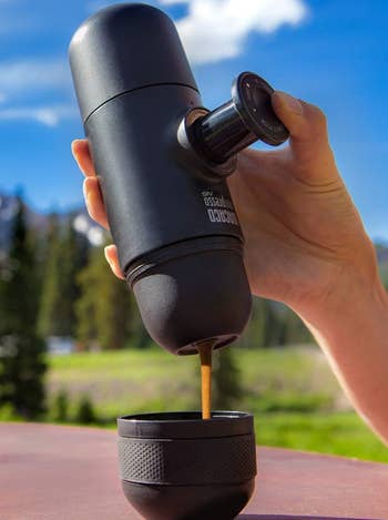 tangan menekan tombol, menunjukkan bagaimana espresso keluar dari bagian bawah pembuat