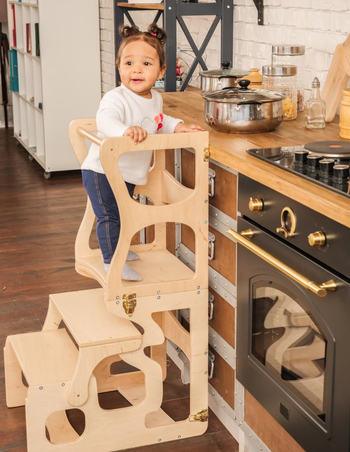 child standing on wooden learning tower in the kitchen