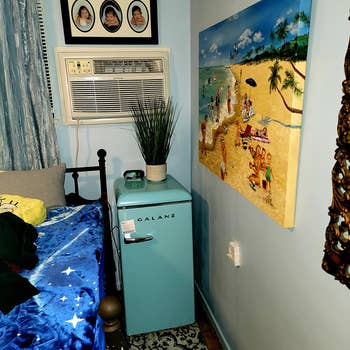reviewer pic of light blue retro-looking mini fridge in a bedroom