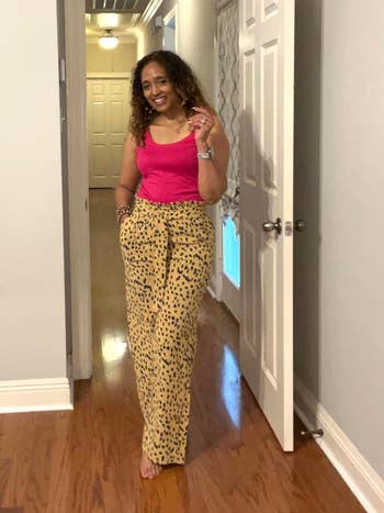 Reviewer standing in a hallway wearing a pink sleeveless top and leopard print trousers, smiling at the camera