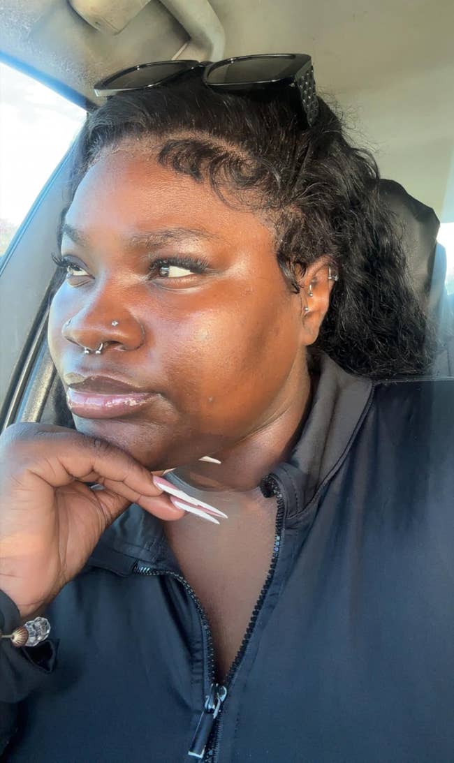 reviewer with agelong nails and sunglasses connected head, sitting successful a car, resting manus connected chin, looking thoughtful