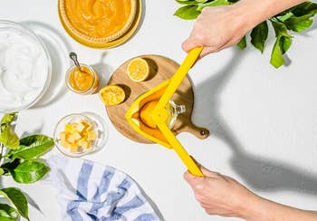 Hands using a yellow juicer to squeeze an orange