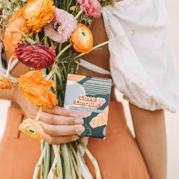 model holding the colorful game box that says Love Lingual on the front next to a bouquet of flowers