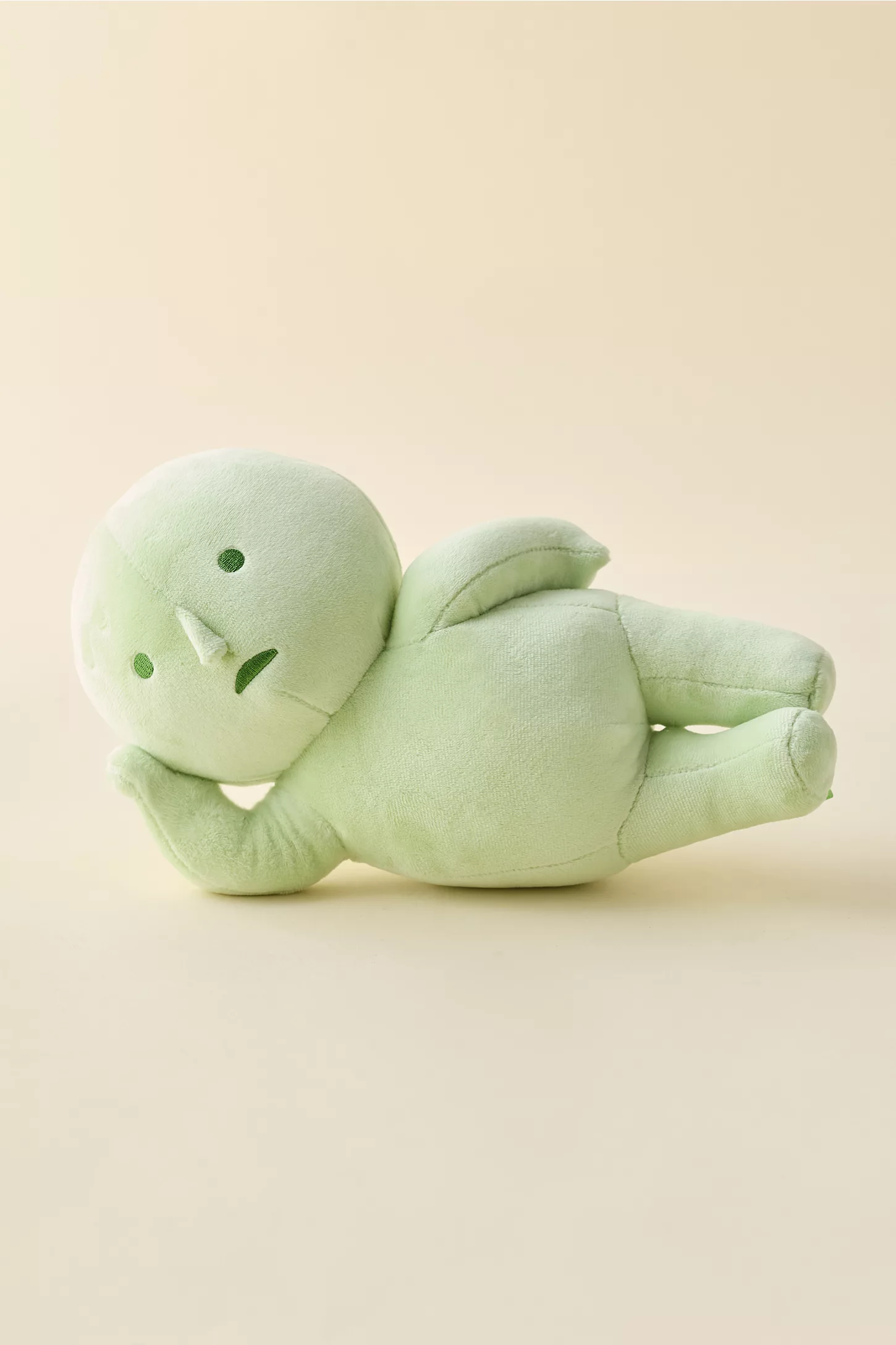 Plush greenish  fig  laying connected  its side, featuring elemental  stitched facial expressions. Soft and minimalistic design, suitable for decor oregon  children