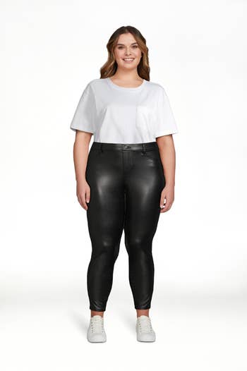 Model wearing black faux leather jeggings with pockets and white tuck in t-shirt with white sneakers