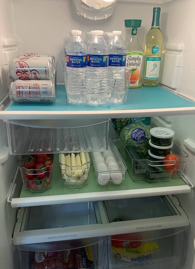 Fridge shelves with items organized in clear plastic bins of various sizes 