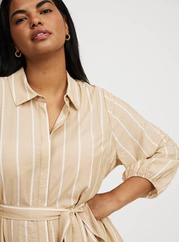 Model wearing a belted shirt dress with vertical stripes, looking confidently at the camera