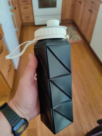 Close-up of a hand holding a black water bottle in extended position