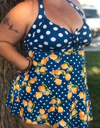Woman in a polka dot and lemon print summer dress stands outdoors by a tree, showcasing the dress fit and pattern