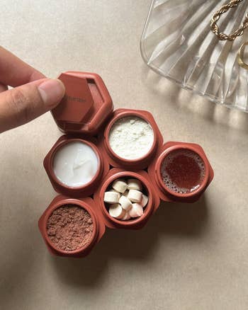 overhead shot of six terracotta containers holding things like pills, skincare products, and powders with model placing a label on one