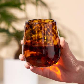 Hand holding a stylish tortoiseshell-patterned solid tumbler, suitable for drinks, with a blurred works and airy background