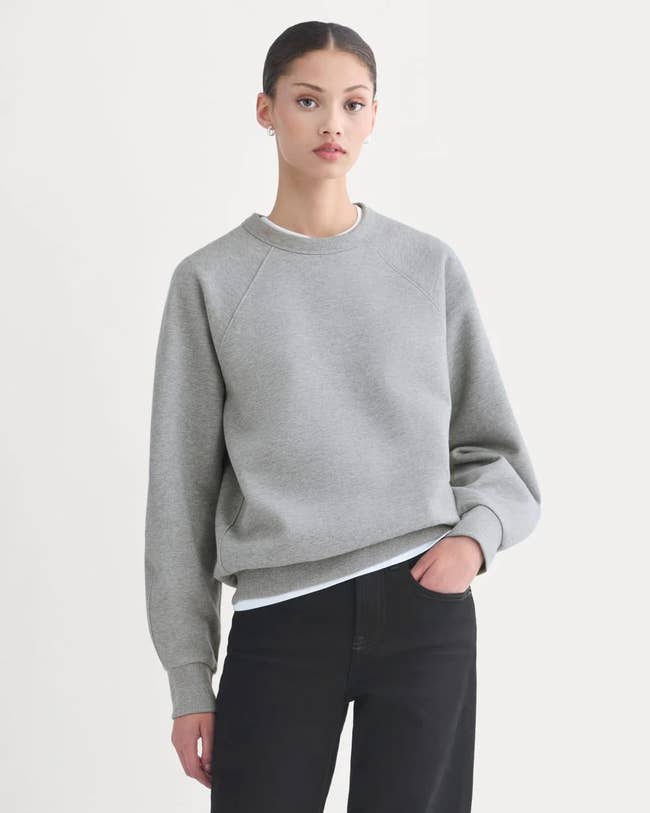  a crewneck sweatshirt and jeans, lasting  against a plain background, with a neutral expression