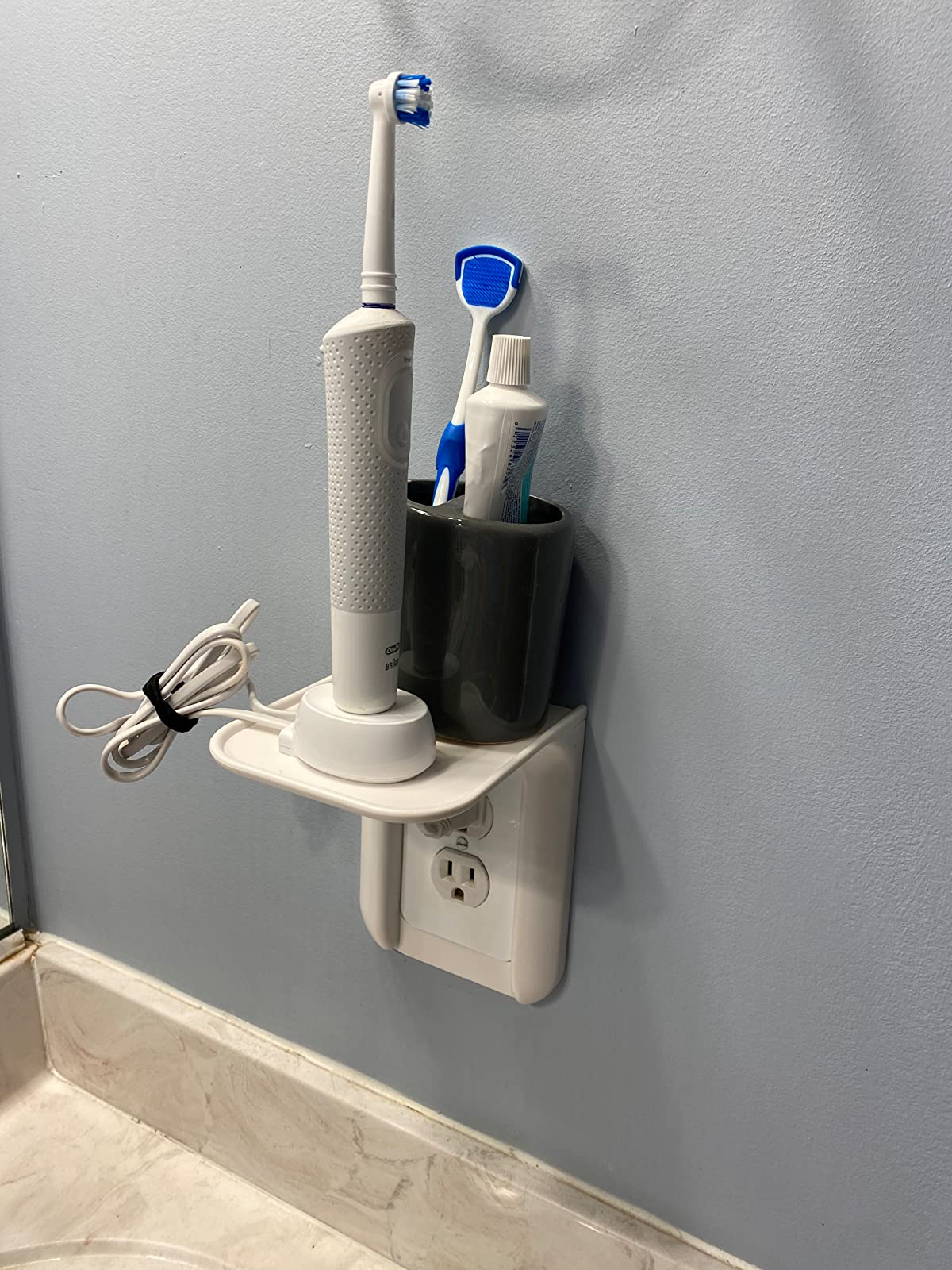 Reviewer photo of white outlet shelf holding electric toothbrush and toothpaste hodler