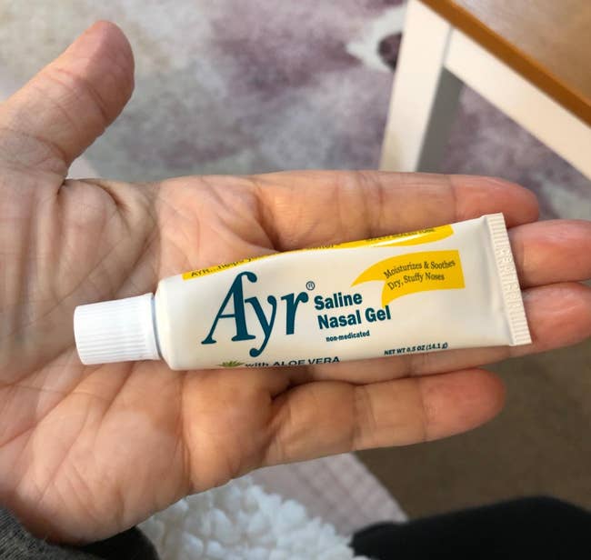 Hand holding a conduit of Ayr Saline Nasal Gel, a moisturizing merchandise for dry, stuffy noses