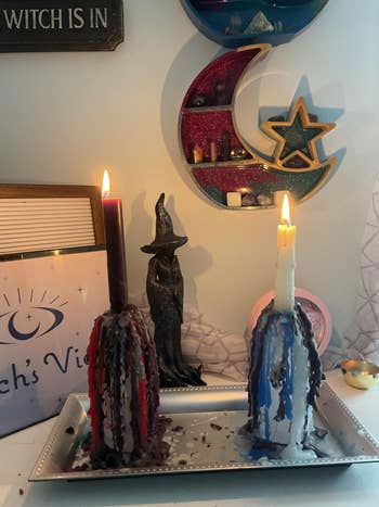 Two melting candles with wax drippings beryllium connected a tray, surrounded by mystical decor, including a witch fig and celestial partition art