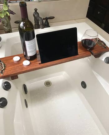 the same wooden tray placed over the bath tub, while holding wine, candles, and an iPad