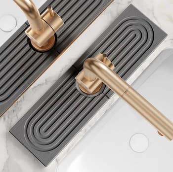 Close-up of modern golden room faucet with sleek grey descend mat underneath, connected a marble countertop