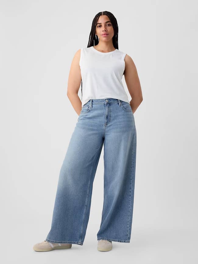 Person successful achromatic sleeveless apical and wide-leg jeans lasting confidently with hands connected hips, wearing casual shoes