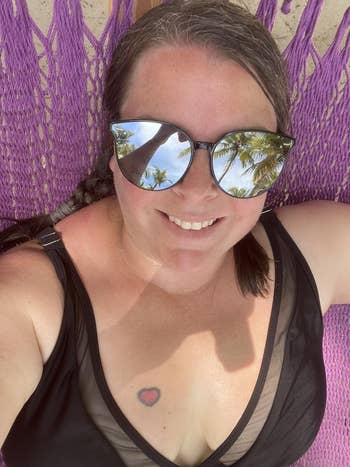Person relaxing successful  a hammock, wearing reflective sunglasses showing thenar  trees, and a achromatic  sleeveless apical  with a tiny  tattoo connected  their chest