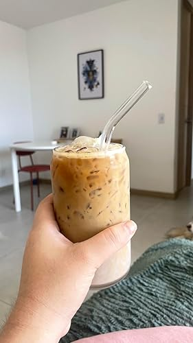 Person holding an iced coffee with a glass straw in a cozy living room setting