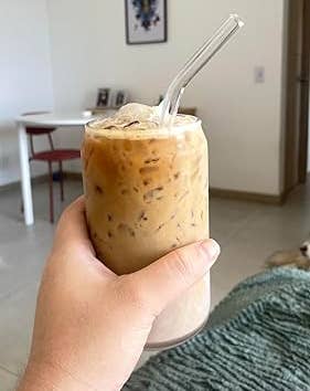 Person holding an iced coffee with a glass straw in a cozy living room setting