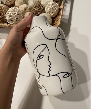 Reviewer holding black and white flower vase with abstract drawings of one line faces