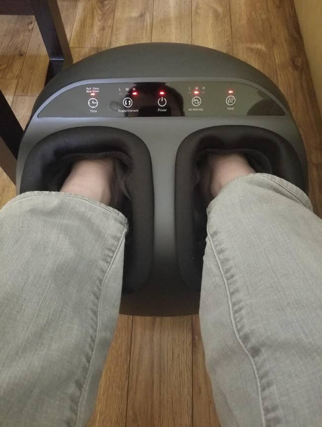 Feet in a foot massager on a wooden floor, showing control buttons for strength, power, air intensity, and heat