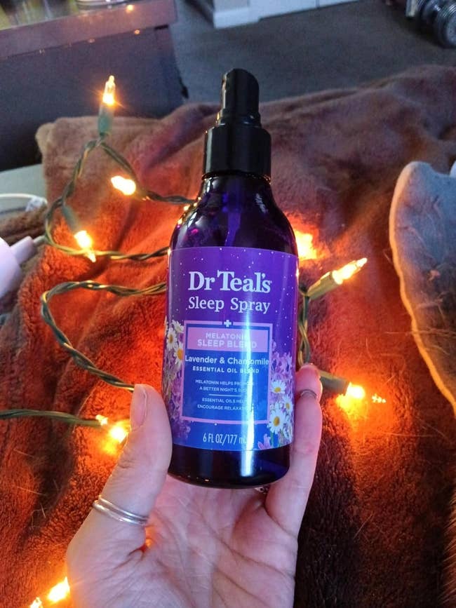 Person holding Dr Teal's Lavender & Chamomile Sleep Spray, surrounded by drawstring lights connected a brushed blanket
